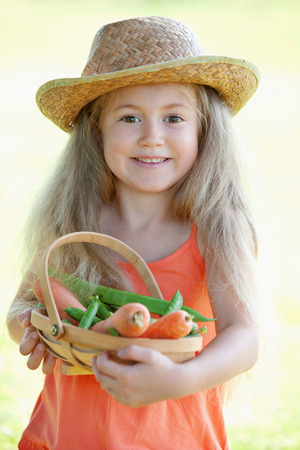 Girl holding a basket of carrots and peasの写真素材