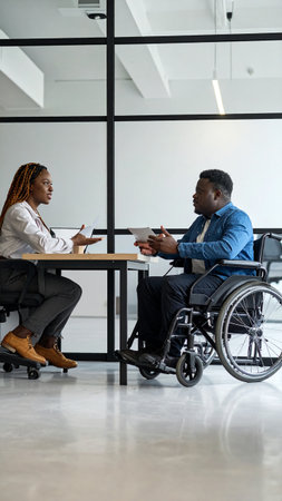 Side view of businessman and businesswoman in wheelchair working together in officeの素材