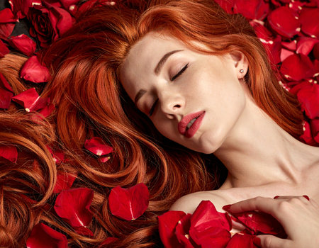 Beautiful redhead girl lying on rose petals. Fashion photo.の素材