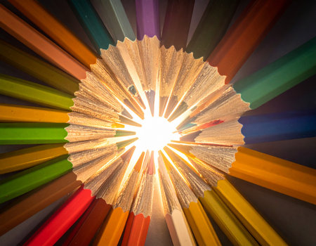 Colorful pencils in the shape of a sun on a black backgroundの素材
