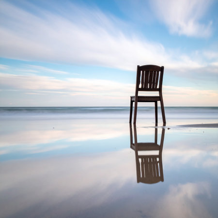 Wooden chair on the beach with reflection of sky and clouds.の素材