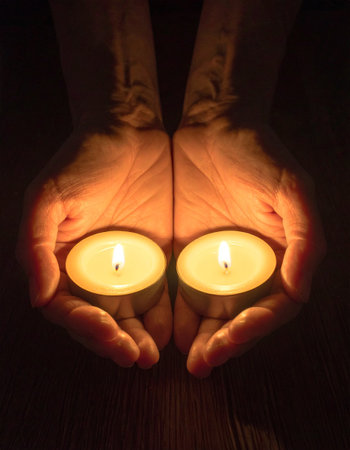 Woman's hands holding burning candles in the dark, close-upの素材