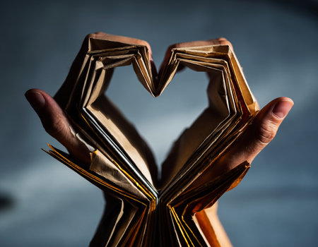 Open book with heart shaped pages in hands on a dark background.の素材