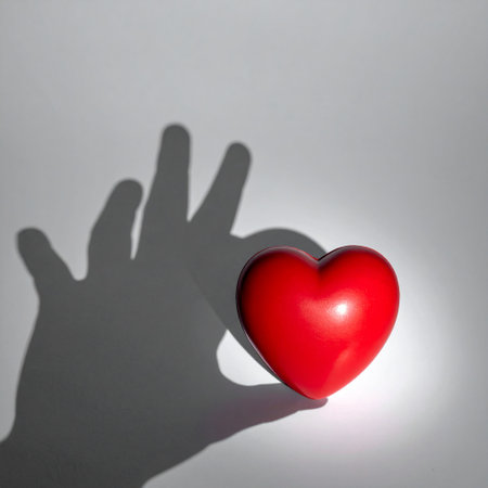 Red heart on a white background with a shadow of a hand.の素材