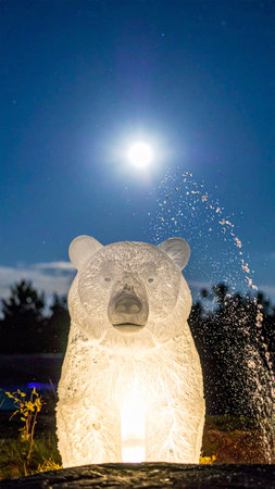 A polar bear drinking water from a fountain at night in the parkの素材