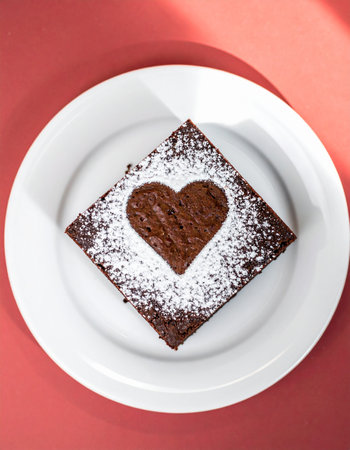 Chocolate brownies with heart shape on top on a red backgroundの素材