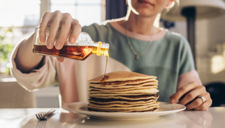 cropped shot of woman pouring maple syrup on stack of pancakes at homeの素材