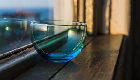 Blue glass bowl on a wooden window sill next to the sea.の素材