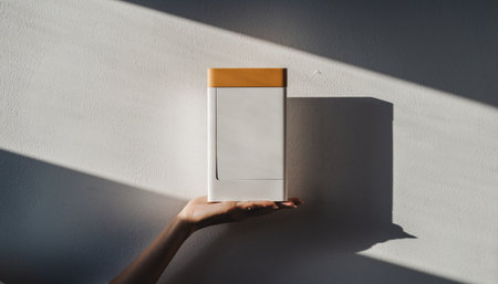 Female hand holding blank paper box with shadow on white wall. Mock upの素材