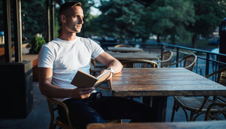 Portrait of a handsome young man reading a book while sitting in a cafe outdoorsの素材