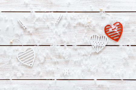 Snowflakes and white red hearts on wooden table, soft flakes of snow on light xmas desk, merry Christmas holiday or romantic Valentines day background card, happy new year, top view from aboveの写真素材