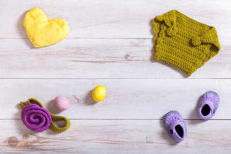 Knitted baby clothes and accessories on white wooden background, newborn handmade clothing set, kid items on table, child fashion for girl boy modern baby shower gift, infant apparel shop, top viewの写真素材