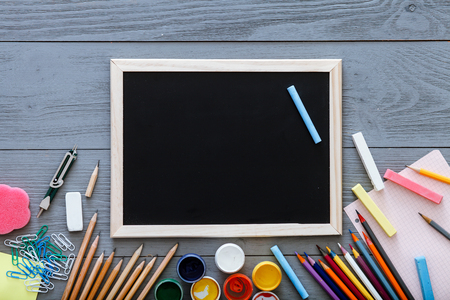 Chalkboard on grey dark desk with colorful pencils, paints, other school supplies for schoolwork, back to school sale concept, creative workplace for new learning year, top view, copy spaceの写真素材
