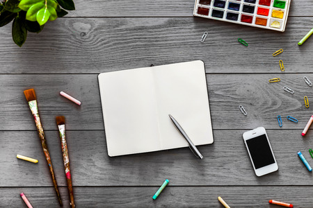 Colorful creative artist table with blank notebook for work sketches and paints, art paintbrushes supplies set on grey wooden background, top view, copy space, flat lay style, drawing class educationの写真素材