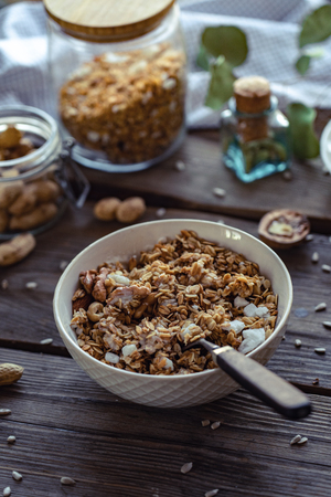 Granola morning breakfast bowl with spoon on brown wooden table background, healthy muesli food concept, cereal meal with nuts seed organic diet oat meal for health care, vertical close up viewの写真素材