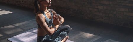 Calm fit sporty healthy mindful woman sit in lotus pose doing yoga exercise breathing fresh air meditating in gym lit with sunlight, stress free concept, horizontal banner website design, copy spaceの写真素材