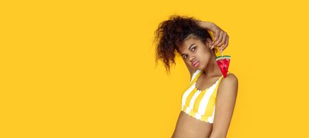 Fashion young african teen girl black woman holding watermelon candy ice cream looking at camera isolated on yellow summer studio background, horizontal banner website design, portrait, copy spaceの写真素材