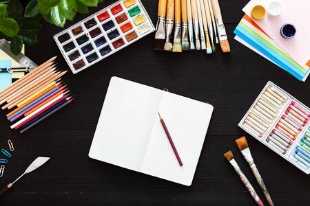 Creative art work table concept, mock up blank notebook sketchbook, paintbrushes set and paintbox for creativity sketches on black wooden drawing background, top view from above, flat lay copy spaceの写真素材