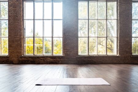 Rolled yoga pilates rubber mat inside gym studio on wooden floor background