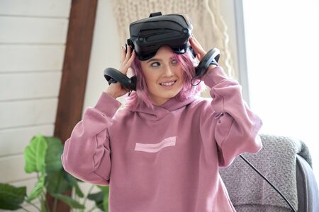 Teen girl pink hair wear vr headset hold controllers experience virtual reality.