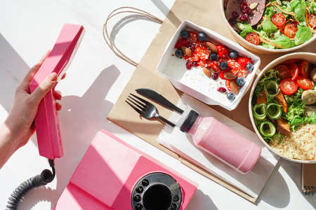 Hand of woman holding telephone receiver near food boxes, meal delivery service.の写真素材