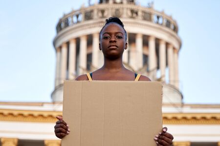 Young african woman activist stand outdoor hold empty sign protesting on street.