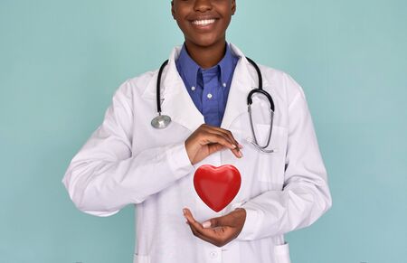 Smiling african female doctor wear white coat holding red heart in hands.の写真素材