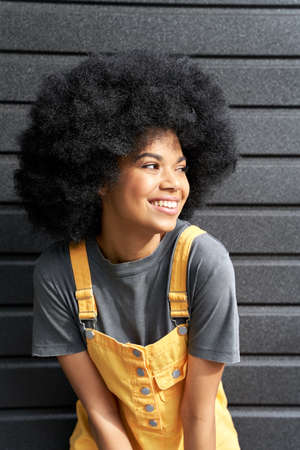 Happy African teen girl with Afro hair laughing standing on black background.