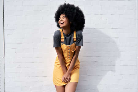 Happy African lady with Afro hair laughing standing against white brick wall.の写真素材