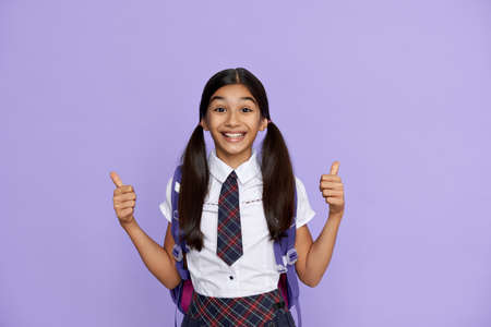 Excited happy indian school girl show thumbs up isolated on violet background.の写真素材