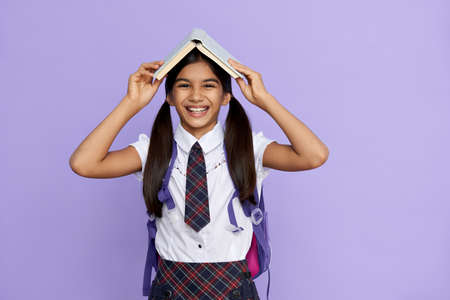 Funny happy indian child primary school girl laughing holding book over head.の写真素材