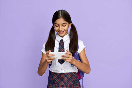 Indian school girl holding phone watching online class isolated on background.の写真素材