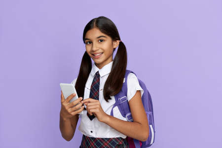 Happy indian kid school girl holding smart phone isolated on lilac background.の写真素材