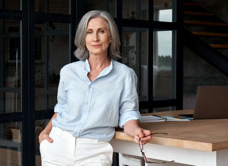 Confident stylish middle aged woman standing at office workplace, portrait.
