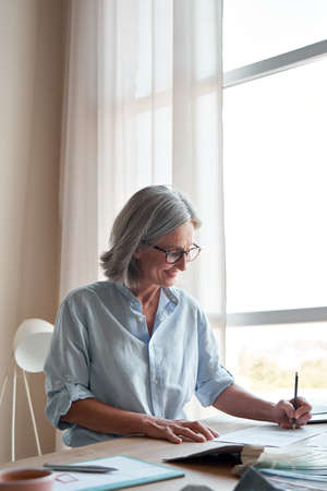 Smiling mature stylish woman fashion designer drawing sketches in modern studio.の写真素材