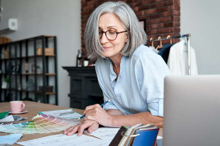Middle aged stylish woman fashion designer drawing sketches in studio office.の写真素材