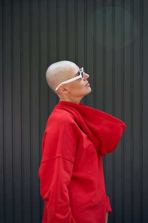 Cool bald woman wearing red hoodie and sunglasses standing on background.の写真素材