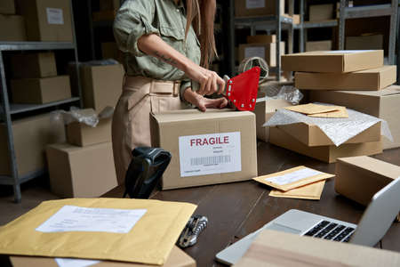 Female post mail storage worker holding tape dispenser sealing shipping box.の写真素材