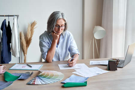 Senior elegant female fashion designer drawing sketches in studio office.