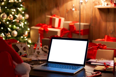 Laptop with white screen on Christmas table with gifts in xmas background.
