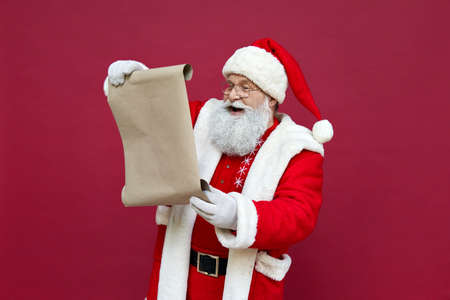 Happy Santa Claus reading wish list isolated on red background.の写真素材