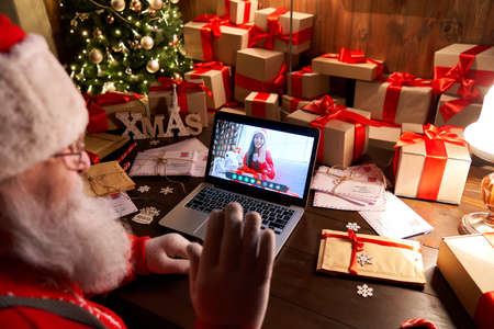 Santa Claus talking to child on laptop video call open present sit at table.