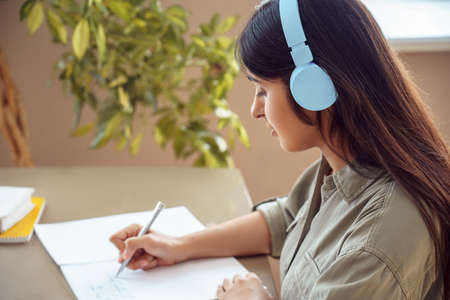Indian woman student wearing headphones writing listening audio course at home.の写真素材