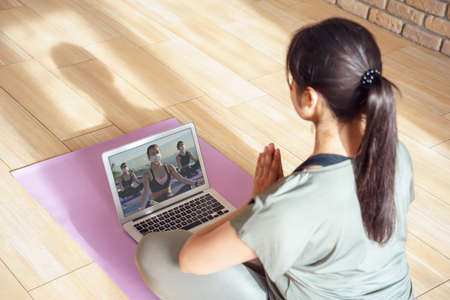 Young woman meditating watching online yoga class video tutorial at home.
