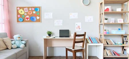 Child room interior space with table, couch, books and laptop on table at home.