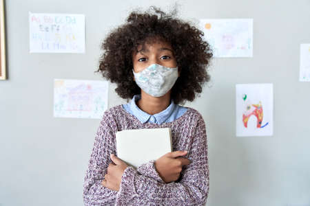 Cute small school pupil african kid girl wears face mask standing in classroom.