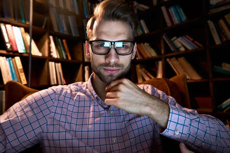 Serious young businessman looking at webcam conference calling watching webinar.