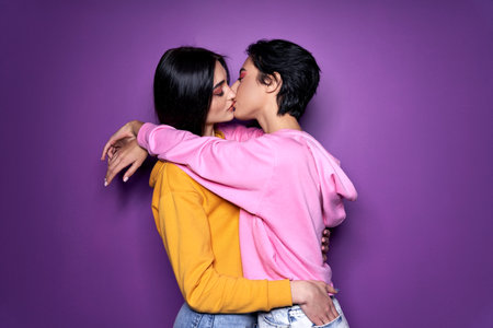 Two girls lesbian couple hugging kissing on purple background.