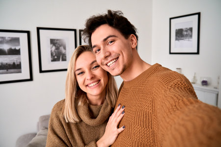 Happy young couple hugging looking at camera taking selfie at home, portrait.の写真素材