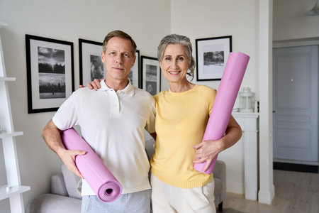 Happy fit old couple hugging, looking at camera, holding yoga mats at home.の写真素材